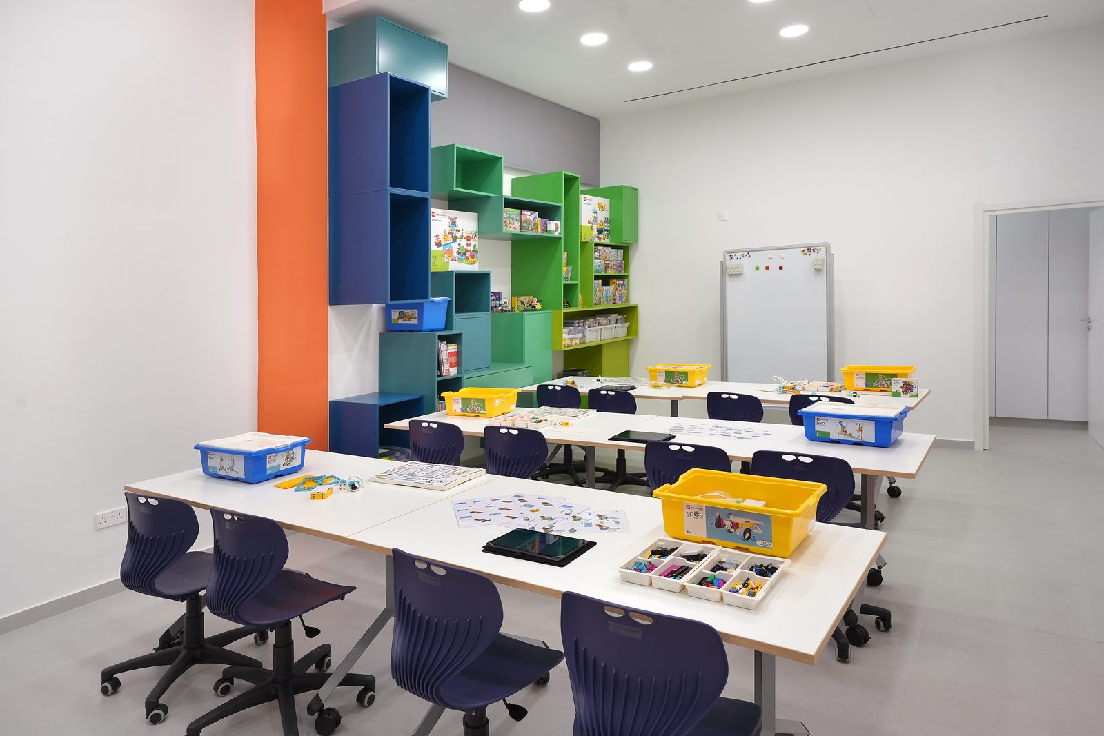 The Stride classroom: white tables with yellow LEGO Education boxes, tablets and navy chairs